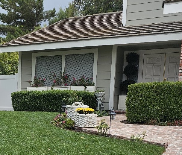 Boxwood hedges trimmed square beneath front windows with flower boxes and entry topiary