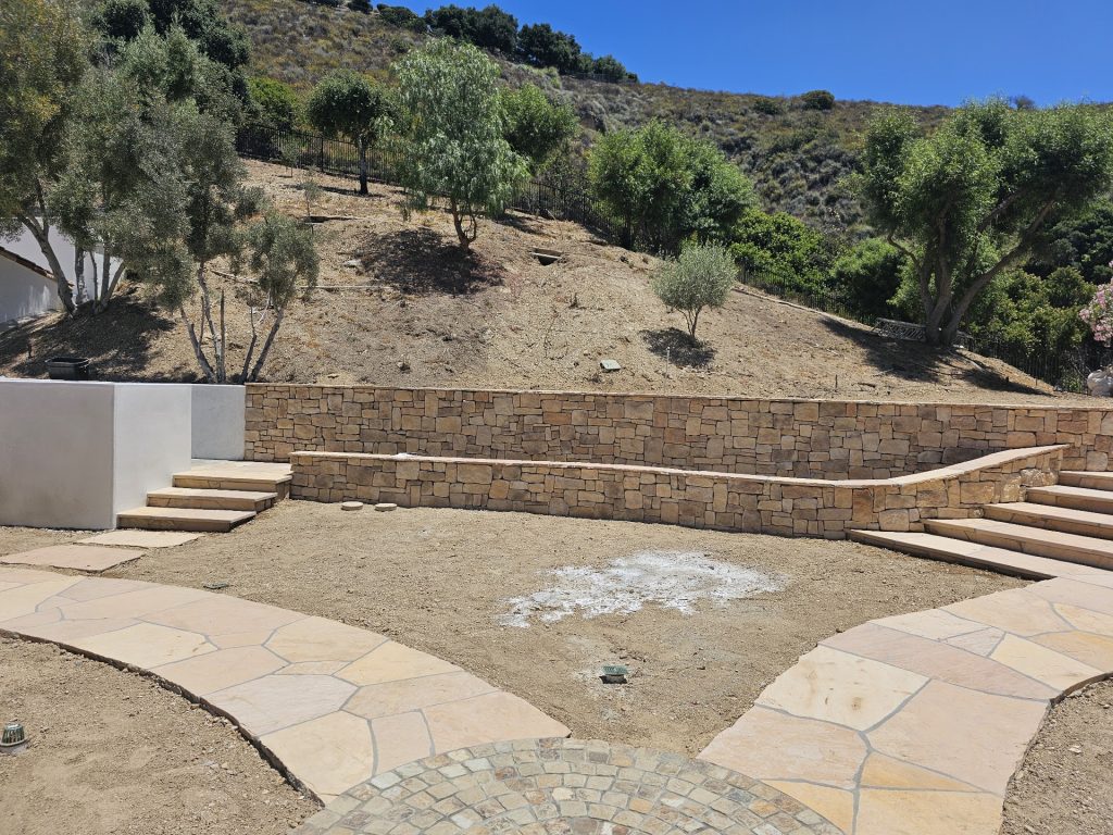 Natural stacked-stone retaining wall with flagstone steps and paths terracing a hillside backyard