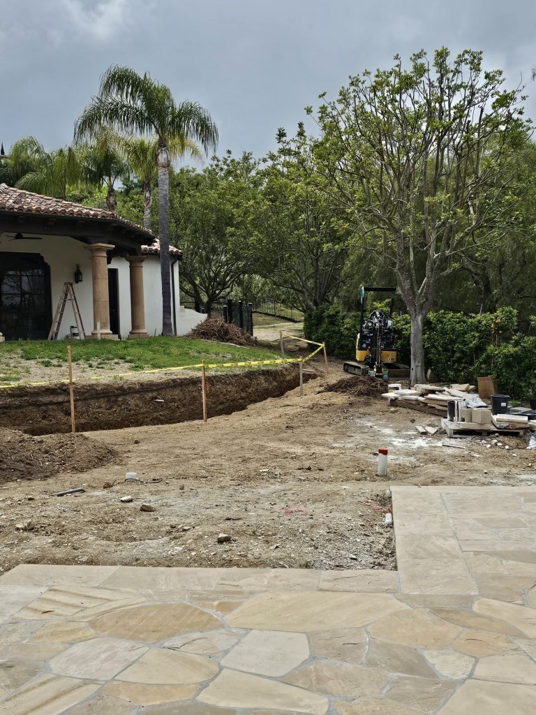 Irrigation trench dug along a hedge border with flagstone pavers staged for a landscape build